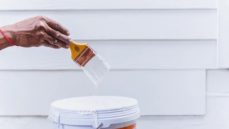 Maalari kastaa pensselin maaliämpäriin